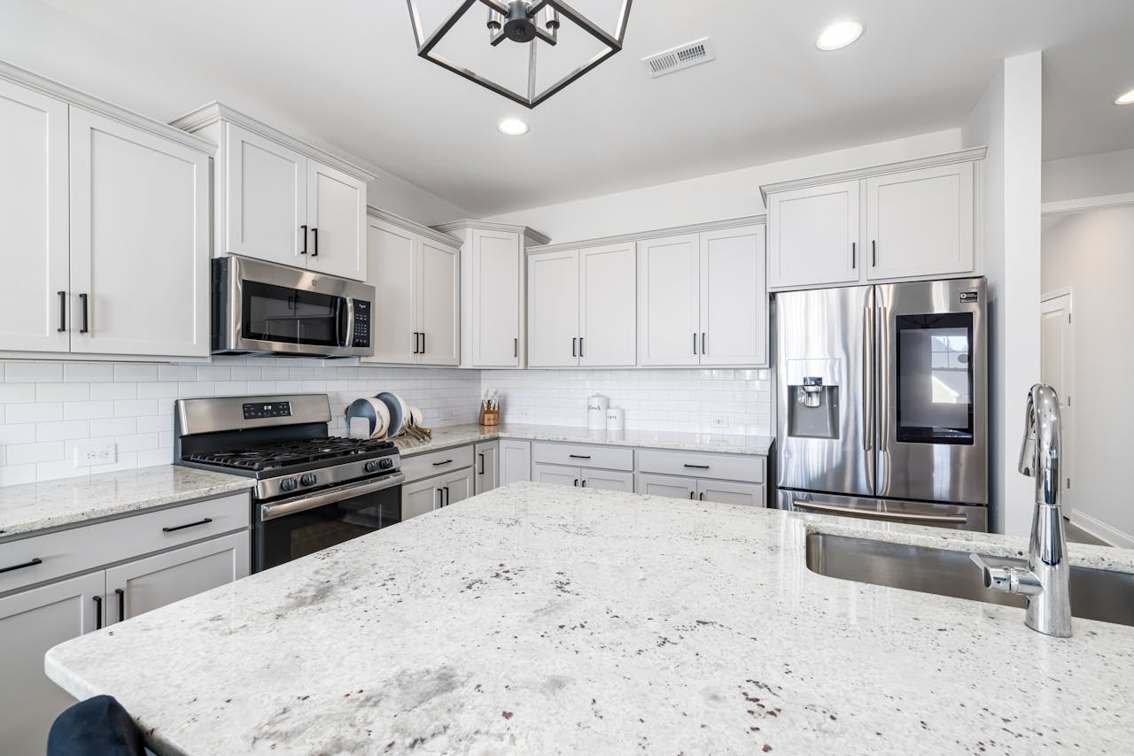Bright and modern kitchen with white cabinets and stainless steel appliances, featuring a granite countertop island.