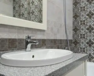 Close-up of a modern white sink and faucet with ornate patterned tiles in the bathroom.