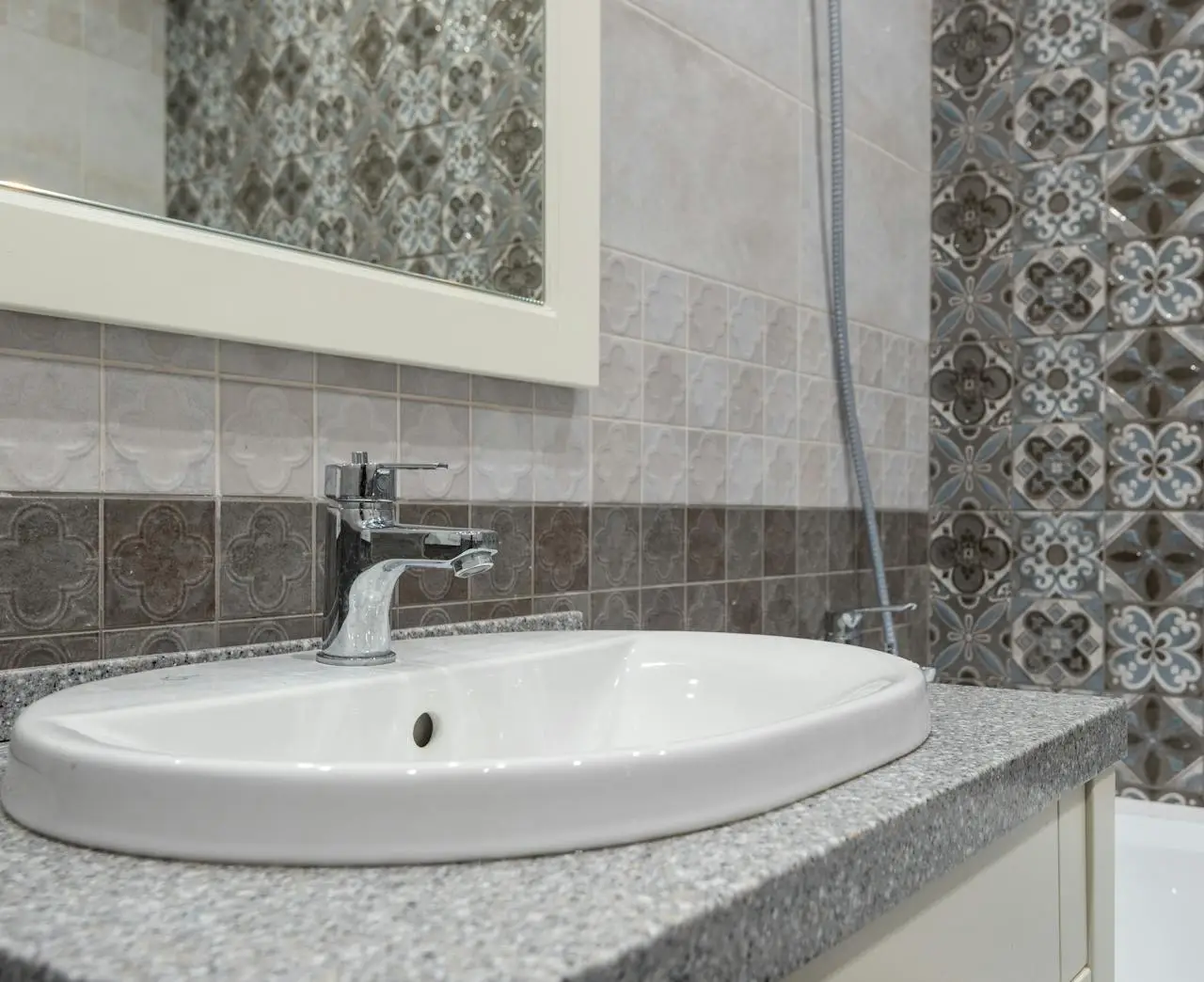Close-up of a modern white sink and faucet with ornate patterned tiles in the bathroom.
